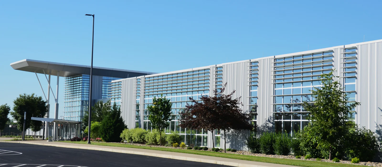 Modern corporate campus building with glass and white metal panels beside landscaped grounds.