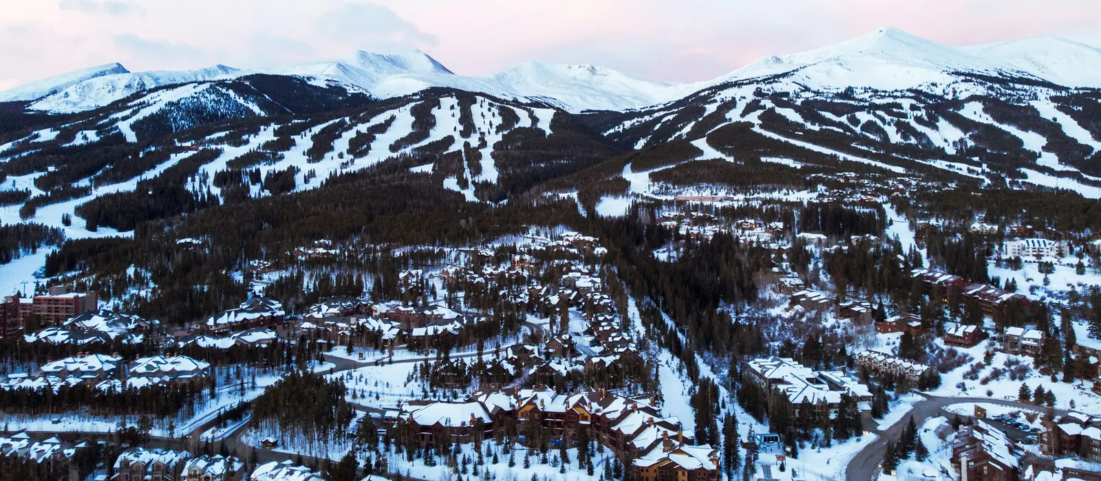 Aerial view of the town of Breckenridge in winter, with the ski resort's snow-covered runs rising behind it.