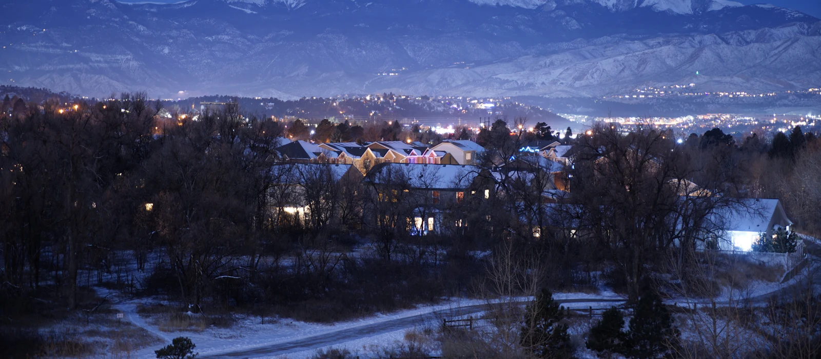Colorado Springs at dusk, snow on the ground and city lights glowing below the mountains.