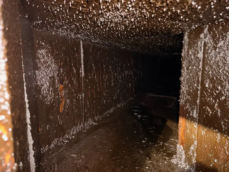 Inside a kitchen exhaust duct, walls and floor coated in brown grease.