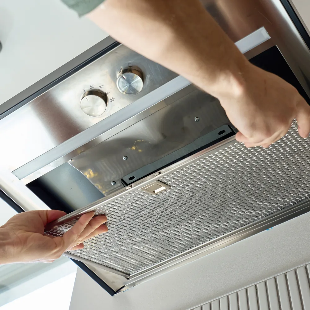 Hands lifting a mesh grease filter out of a stainless hood.