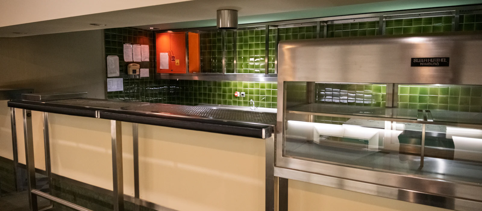 Commercial kitchen with a green tile backsplash, stainless counters, and a pass-through shelf.