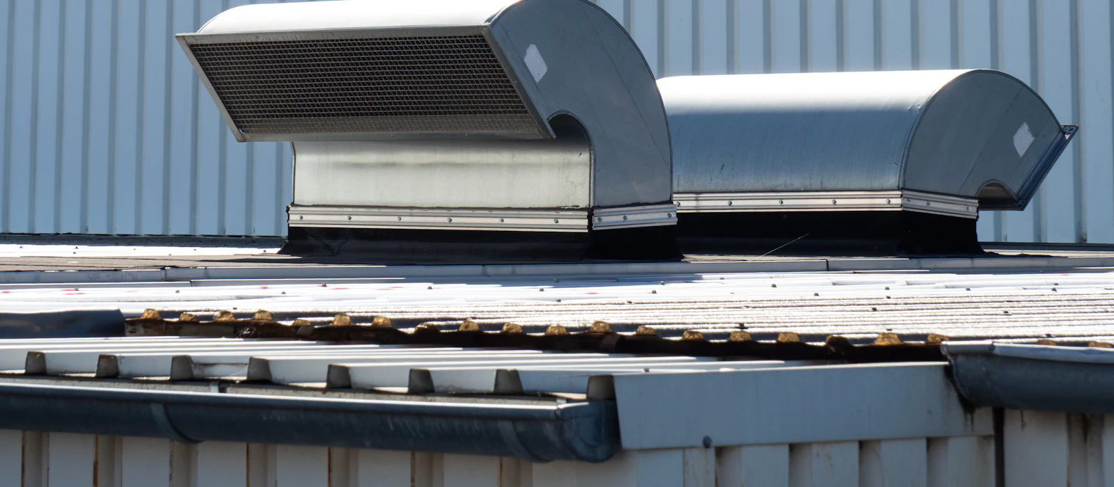 Stainless steel rooftop exhaust ducts and vented fan housings on a metal-roofed building.