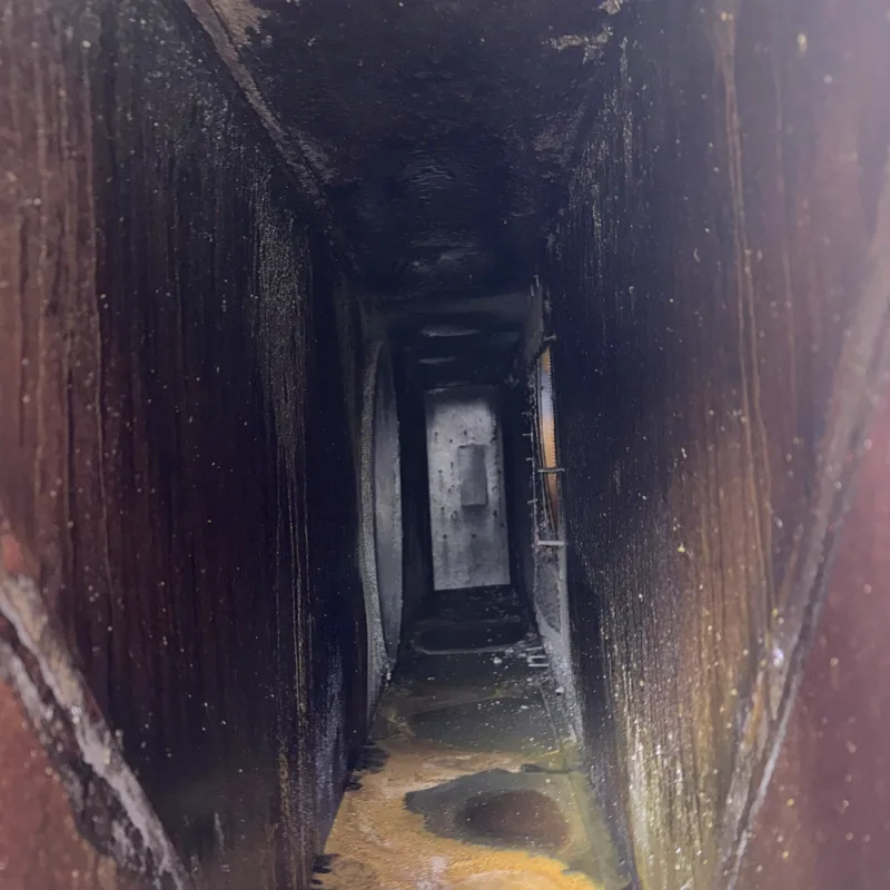Hotel kitchen exhaust duct before cleaning, dark grease on the walls and pooled at the base, Cheyenne, Wyoming.